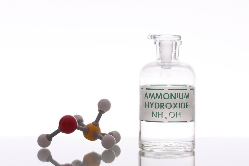A glass reagent bottle labeled 'AMMONIUM HYDROXIDE NH₄OH' sits next to a ball-and-stick molecular model