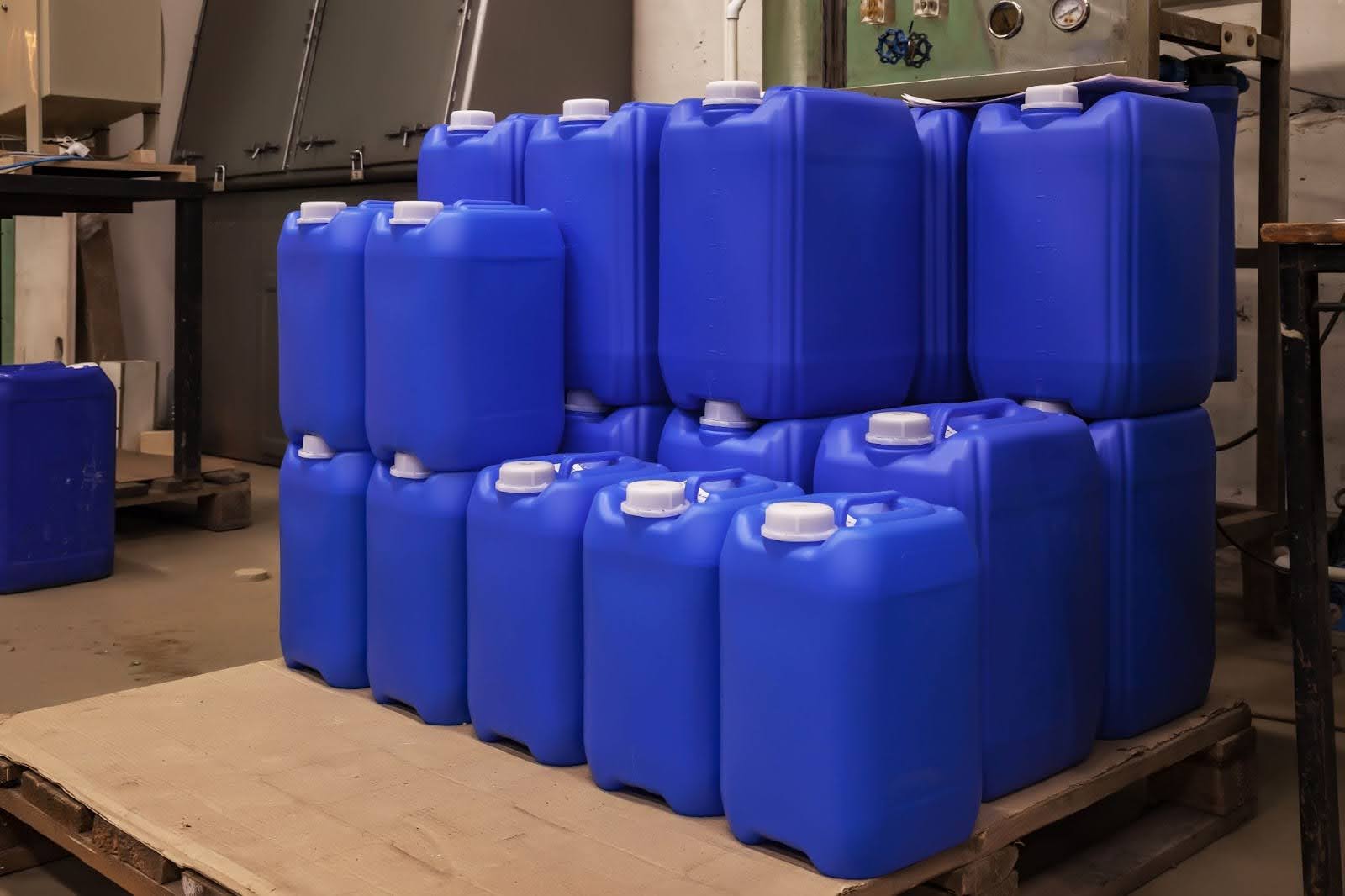 A stack of blue plastic jerrycans with white screw caps resting on a wooden pallet