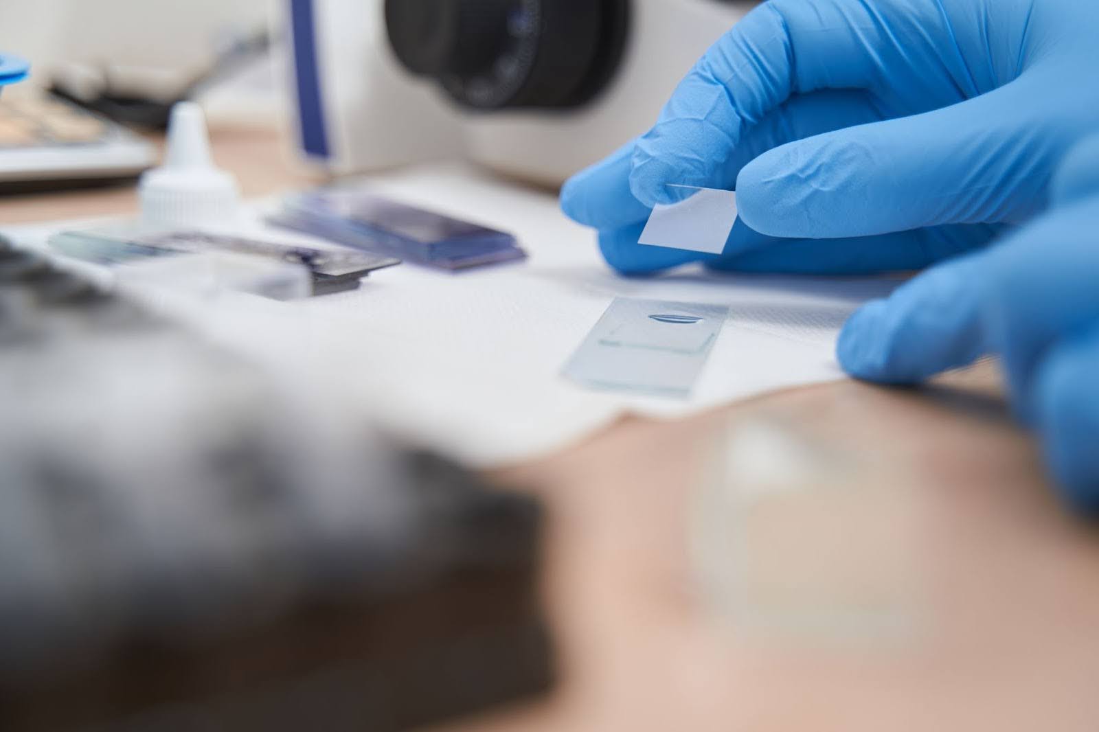 close-up of a scientist's hands in blue gloves carefully placing a coverslip over a specimen on a glass microscope slide in a laboratory
