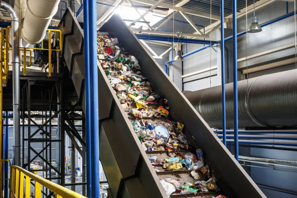 A massive stream of unsorted garbage and recyclables moving through an industrial recycling center machinery